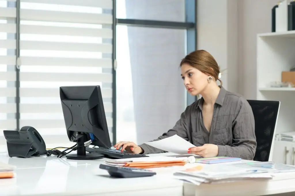 Young woman focused on computer and documents at office desk.
